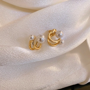 Macro shot of gold double-layer C-shape earrings with pearls on white silk