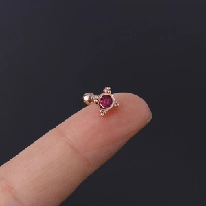 Detailed close-up of a tiny rose gold ear stud with pink zircon on a fingertip
