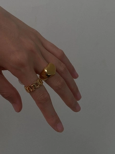 Detailed close-up of a golden heart signet ring and a hollow chain link band worn on hand