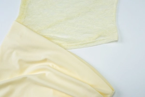Detailed view of pale yellow lace patchwork and glossy silk-like fabric on the dress