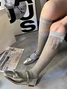 Detail of grey ribbed knit knee-high socks with delicate bow and silver Mary Jane shoes
