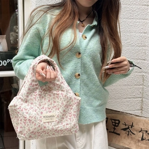 Floral canvas lunch bag with branding label held by a model against a white brick wall