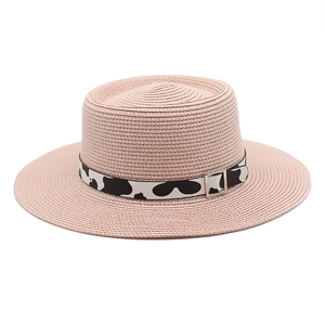 Detail of pink straw boater hat featuring cow print ribbon and silver buckle