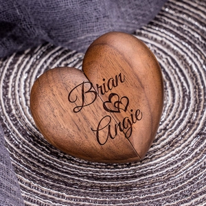 Detailed heart-shaped walnut ring box with custom laser engraving on a woven mat