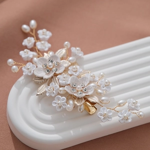 Elegant gold hair comb with white ceramic flowers, pearls and crystals on beige fabric