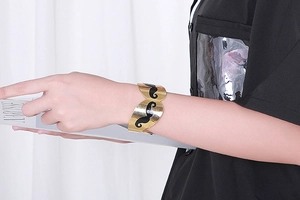 Close-up of gold cuff bracelet featuring a black mustache pattern on a female model