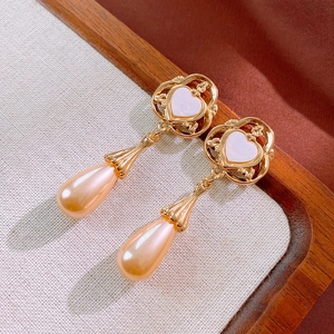 Détail de boucles d'oreilles cœur vintage avec perles roses et gravure florale dorée