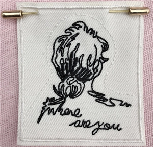 Detailed embroidery on white fabric brooch with 'Where are you' text and golden pins