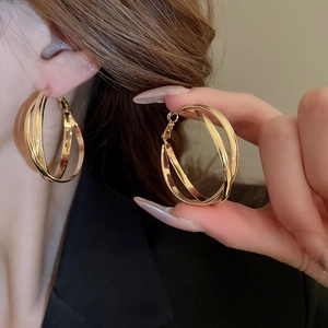 Detail view of large multi-layer gold plated hoop earrings on model's ear showing shiny finish