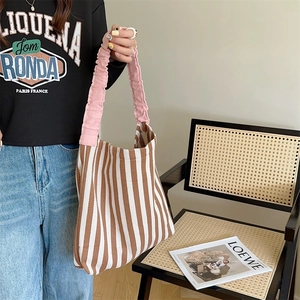 Detail of canvas tote bag featuring brown stripes and pink pleated shoulder strap