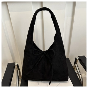 Detail of black faux suede tote bag featuring a decorative bow on a modern chair