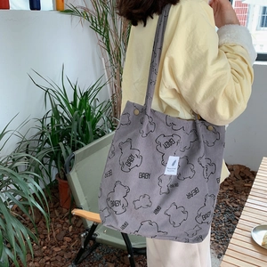Detail of dark gray corduroy tote bag featuring bear embroidery on a model in outdoor setting
