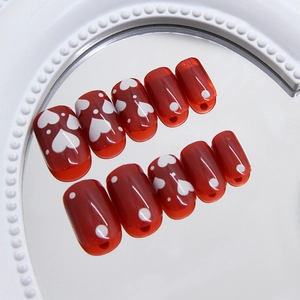 Burgundy heart pattern press-on nails with white dots on a decorative mirror surface