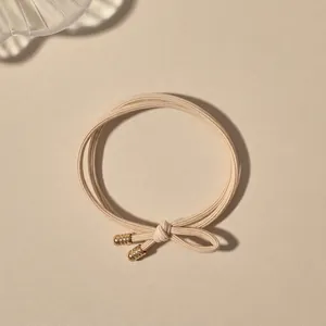 Detail of beige braided elastic hair tie with elegant gold spiral metal hardware