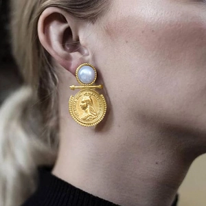 Close-up of vintage gold coin earrings with pearls worn by a model on stainless steel