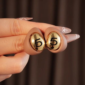 Close-up of gold-plated drop earring with light brown matte frame and black number 5