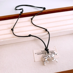 Macro detail of zebra pendant necklace with black wax rope on woven texture background