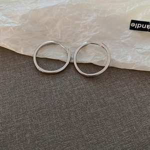 Detailed close-up of minimalist silver round hoop earrings on a textured paper background