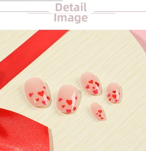 Detail of nude pink press-on nails with red heart patterns and glossy finish