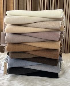 Sciarpe in cashmere impilate in toni neutri con dettagli di nappe su una coperta