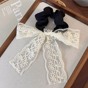 Detail of a black scrunchie with a detachable cream floral lace bow on a wooden tray