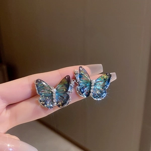 Détail macro de boucles d'oreilles papillon avec ailes irisées, perles et cristaux fins