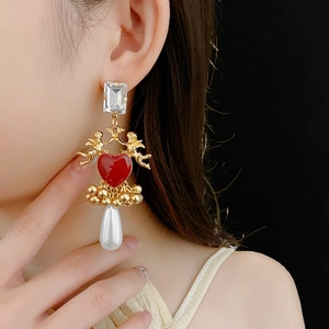 Detail of vintage baroque earrings with gold angels, red hearts, and pearl tassels