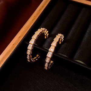 Detailed view of golden hoop earrings with snake scale texture and sparkling zircon pave