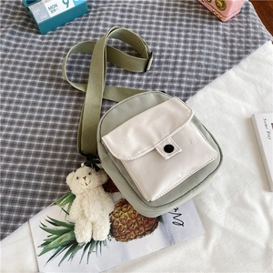 Détail du sac bandoulière en toile vert et beige avec charm ours en peluche sur tissu