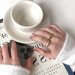 Gold wavy band and white enamel ring set worn by model in a minimalist setting
