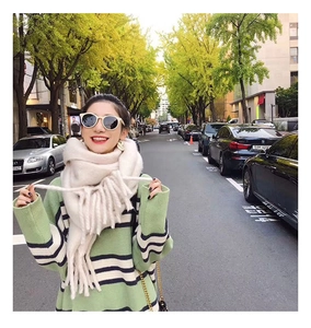 Detail of soft beige faux cashmere scarf with long tassels paired with a green striped sweater