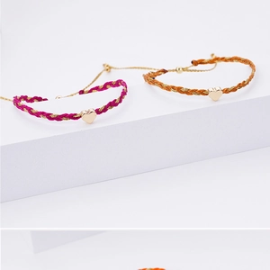 Detail of woven friendship bracelets in rose and orange with gold heart charms