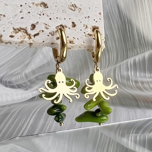 Detailed shot of gold octopus earrings with green stone pendants on stone surface