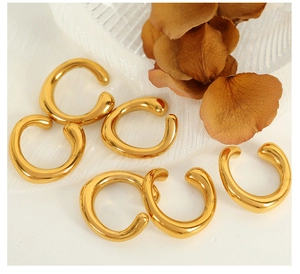 Detail of golden irregular C-shaped ear cuffs on white fabric with dried flowers