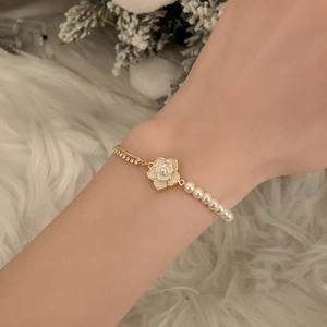 Elegant camellia bracelet with white pearls and gold chain shown on a woman wrist