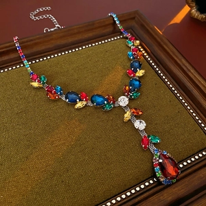 Vintage Y-shaped necklace with colorful crystals on green velvet in a wooden frame