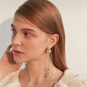 Close-up of elegant gold tassel earrings with pearls on a model against a white wall