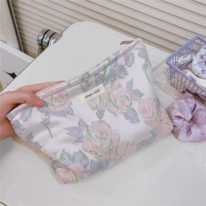 Detail of floral jacquard satin makeup bag with pink rose patterns and brand tag