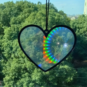 Close-up of heart-shaped suncatcher prism reflecting rainbow colors against green trees