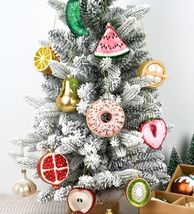 Detailed view of colorful glass fruit and food ornaments hanging on a snowy Christmas tree