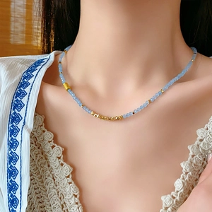Gros plan sur un collier de perles bleu clair avec détails dorés sur un modèle