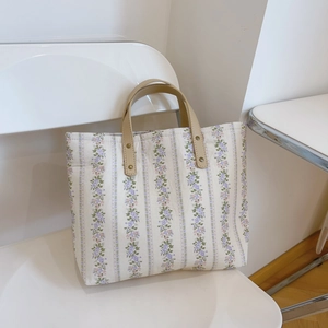 Floral canvas tote bag with purple flower patterns and brown leather handles in a minimal setting