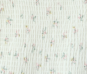 Detail van gesmokte stof met roze en gele bloemen op een witte textielachtergrond