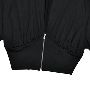 Close-up of silver zipper closure and pleated fabric detail on a black tracksuit set