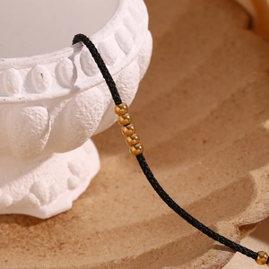 Close-up of black braided cord anklet with 25 small 18K gold plated stainless steel beads