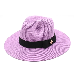 Detail of purple straw fedora hat featuring a black ribbon and golden bee emblem accessory