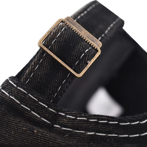 Detail of vintage bronze metal buckle and white stitching on a washed denim baseball cap