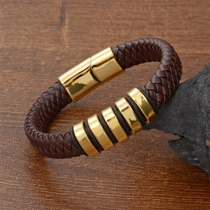Detail of brown braided leather bracelet with gold magnetic clasp on dark rock surface