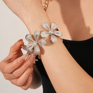 Detail eines silbernen Blumenarmbands mit Strass und texturierten Blüten auf der Haut