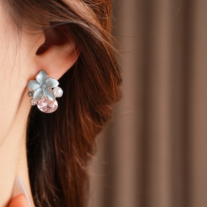 Gros plan d'une boucle d'oreille fleur en émail bleu avec gemme rose et perle blanche